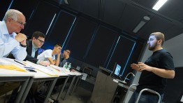 Stan Lapidus (l) and other judges consider the work of  Daniel Galperin (r) and his team's physical therapy device